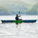 Person kayaking on a calm lake with green mountains in the background