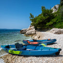 Two blue inflatable kayaks on a pebbly beach with clear blue water and greenery in the background.